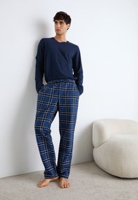 Tricou cu mânecă lungă de culoare bleumarin, asortat cu pantaloni de pijama cu model tartan albastru, cu talie elastică. Material moale, croi lejer, design minimalistic.