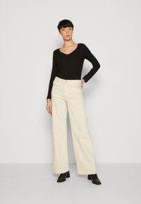 Black long-sleeve V-neck top paired with high-waisted cream wide-leg trousers and black heeled boots, displayed against a neutral background.