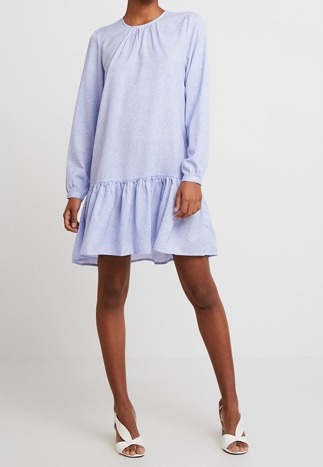 Světle modré šaty s dlouhým rukávem, kulatým výstřihem, strukturovanou tkaninou a volánkovým lemem, zdobené malým bílým květinovým vzorem.