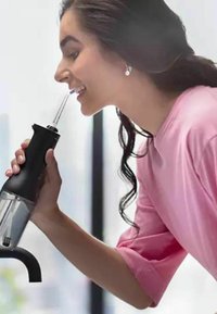 Zwarte handblender met een doorzichtige container, rubberen grip en een flexibele rietje, vastgehouden door een persoon in een roze shirt.