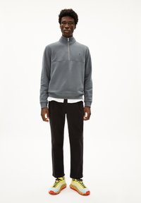 Felpa grigia in pile con zip a metà, pantaloni neri e sneaker gialle con accenti rossi. Design semplice con una vestibilità rilassata e strati a contrasto.