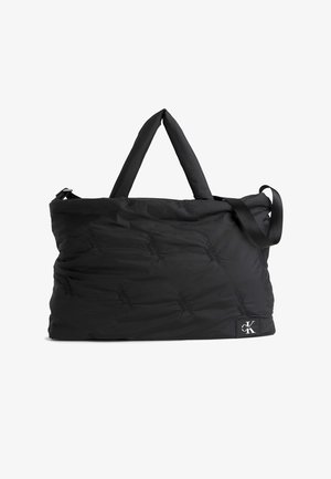 Czarna pikowana torba typu duffel z uchwytami u góry, regulowanym paskiem na ramię oraz małą naszywką z logo Calvin Klein w dolnym rogu.