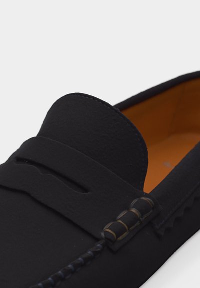 Μαύρο δερμάτινο μοκασίνι με λεπτομερή ραφή, λουρί στο πάνω μέρος και ταμπά εσωτερική επένδυση.