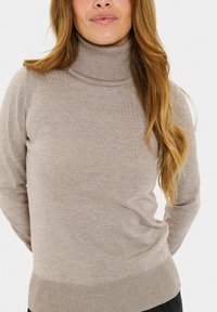 Pull en col montant beige en maille douce, avec un col et un ourlet côtelés, un design ajusté et des manches longues.
