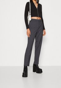 Avskuren svart långärmad topp med dragkedja; grå skräddarsydd byxa; svarta plattform ankelstövlar. Metalliska detaljer på handväskan.