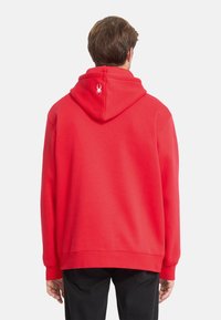 Sweatshirt à capuche rouge avec une coupe décontractée et une poche kangourou. Présente un logo de spider blanc au dos. Fabriqué en tissu doux et texturé.