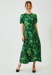 Grön blommig maxiklänning med korta puffärmar, med livfulla mönster av blad och blommor, i varierande nyanser av grönt och svarta accenter.