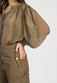 Olivgrünes, transparentes Bluse mit gepufften Ärmeln, knöpfbarem Vorderteil und gerafften Schultern. Kombiniert mit Cargo-Hosen mit Druckknopf-Taschen.