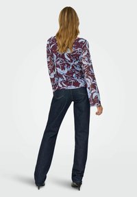 Langærmet, gennemsigtig top med et marmor og lyseblåt blomster mønster, parret med mørkeblå tætsiddende jeans og højhælede sorte sko.