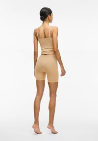 Beige set bestaande uit een aansluitend tanktop en shorts, gemaakt van rekbare stof. Kenmerkt zich door dunne bandjes en shorts tot halverwege de dijen, naadloos ontwerp.