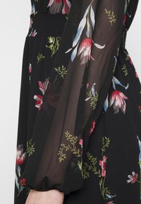 Robe noire à fleurs avec des manches transparentes, ornée de motifs floraux rouges, bleus et verts. Texture douce, détails de poignets et de taille élastiques.