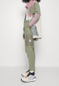 Fleece jacket in green, pink, and cream with front pocket and fleece joggers. Beige and black athletic shoes with grey accents.