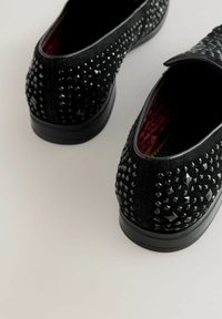 Schwarze Filz-Slipper zeichnen sich durch ein genietetes Design und eine strukturierte Oberfläche aus. Das Innere zeigt ein bordeauxrotes Futter, das die Gesamtästhetik unterstreicht.