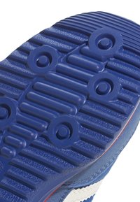 Semelle de chaussure en caoutchouc bleu avec des stries texturées et des motifs circulaires. Présente une bande blanche et des coutures consolidées le long du bord.