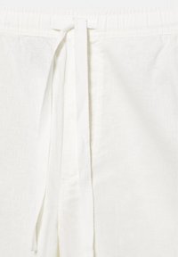 Bele lanene hlače z bombažnim vrvico za zavezovanje na elastičnem pasu, prikaz teksture in šivov.