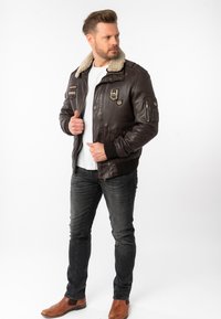 Bruine leren jas met een nepbont kraag, voorzien van patches, ritszakken en geribde boorden, gecombineerd met donkere jeans en bruine laarzen.
