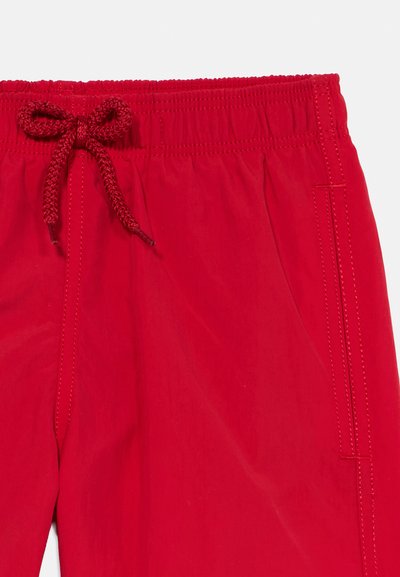 A piros zsinóros nadrág elasztikus derékpánttal, fonott megkötővel, sima textúrával és varrott oldalzsebekkel rendelkezik.