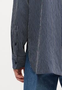 Μπλούζα με ναυτικές ρίγες, διαθέτει λευκές κάθετες γραμμές, κουμπωτές μανσέτες και χαλαρή εφαρμογή. Το ύφασμα έχει υφή.