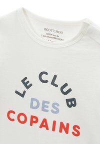 T-shirt en coton blanc avec un texte incurvé en bleu foncé, bleu clair et rouge qui dit "LE CLUB DES COPAINS." Col rond.