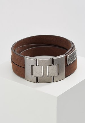 Ceinture double-tour en cuir marron avec une large boucle rectangulaire en métal brossé et de petites étiquettes métalliques à l'extrémité de la lanière.