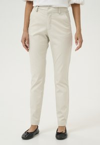 Jasno beżowe spodnie o dopasowanym kroju, z paskami na pasek, dwoma przednimi kieszeniami i gładką teksturą. Noszone z czarnymi balerinami.