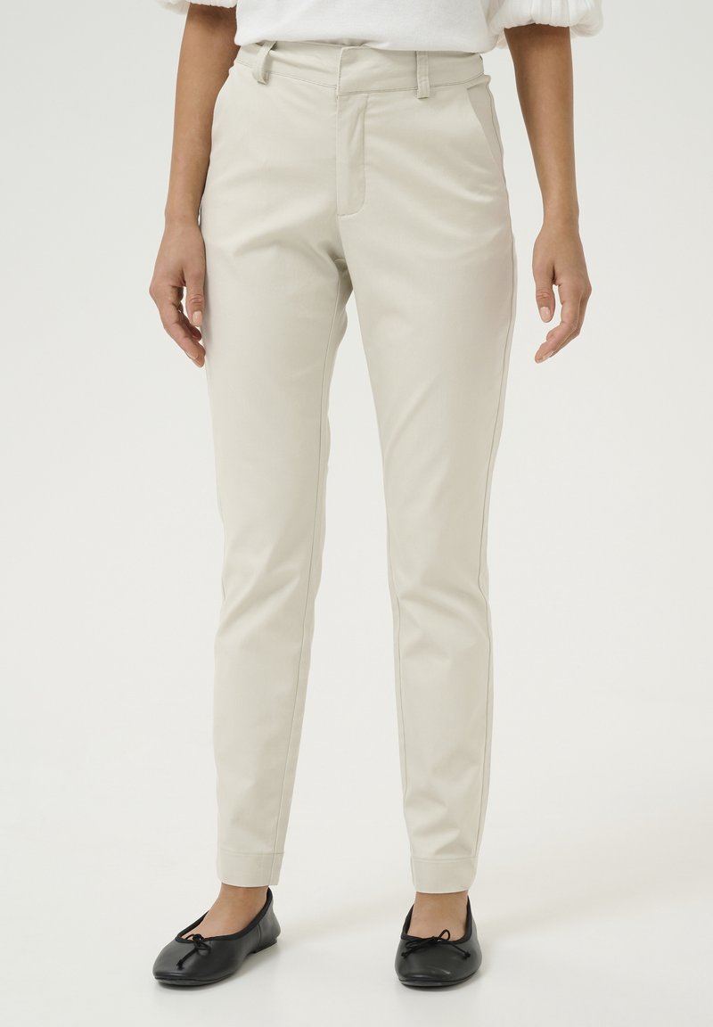 Jasno beżowe spodnie o dopasowanym kroju, z paskami na pasek, dwoma przednimi kieszeniami i gładką teksturą. Noszone z czarnymi balerinami.
