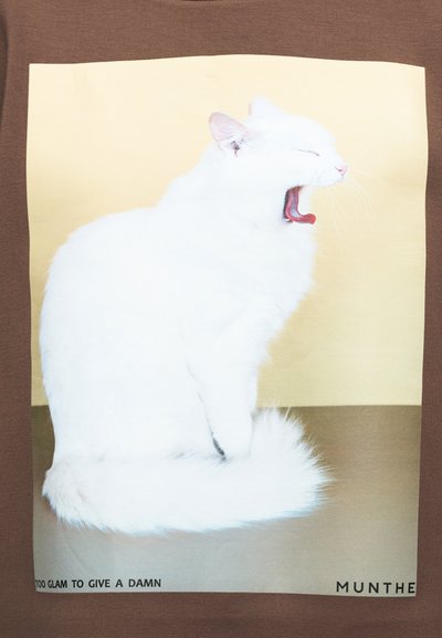 Λευκή γάτα καθισμένη και χασμουριέται πάνω σε μπεζ φόντο, με το κείμενο «Too glam to give a damn» και «Munthe» στο κάτω μέρος.