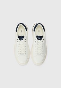 Hvite lær sneakers med marineblå detaljer, flate lisser, rund tå og gummisåle. Har merke-logo på tungen og siden.