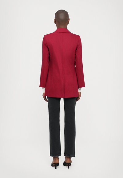 Red long blazer with a tailored fit, notched collar, and long sleeves, paired with black fitted pants and open-toe heels.