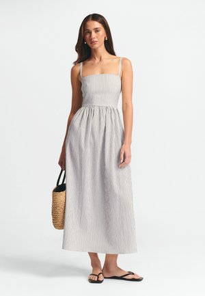 Robe maxi rayée avec un corsage ajusté, une jupe évasée et des bretelles fines. Fabriquée en tissu léger ; la palette de couleurs comprend du blanc et du gris.
