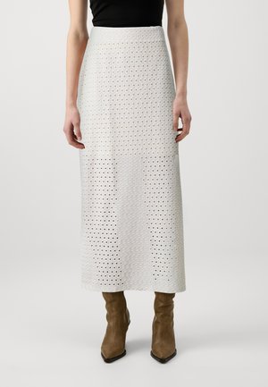 Vit, knälång kjol med geometriskt utskärningsmönster, slät textur, hög midja och matchad med bruna klackstövlar.