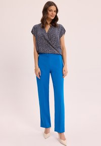 Niebieskie spodnie o prostym kroju w połączeniu z topem w stylu owijanym, wzorzystym, z krótkimi rękawami i dekoltem w kształcie litery V, wykonanym z lekkiego materiału.