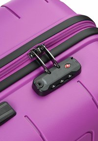 Valigia rigida viola con superficie testurizzata, zip nera e lucchetto approvato TSA. Dotata di maniglia superiore e dettagli resistenti.