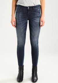 Tummansiniset skinny-farkut, joissa on hieno fading ja risaiset yksityiskohdat. Yhdistetty mustiin nilkkabootseihin.