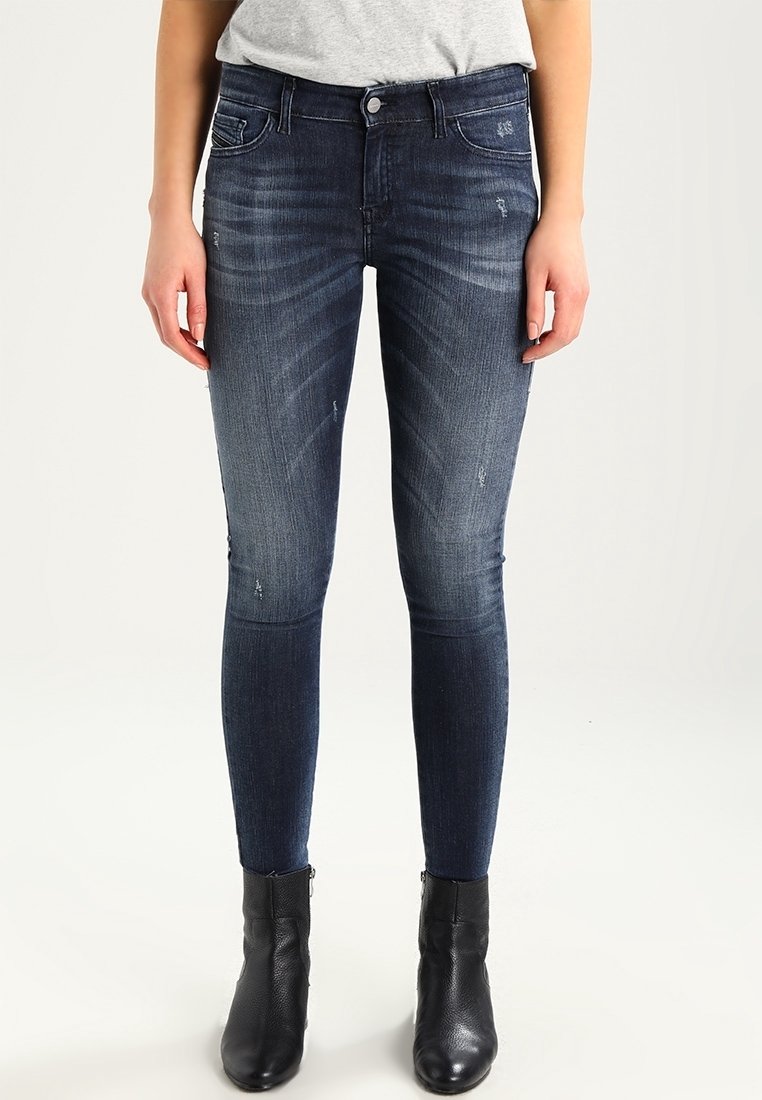 Tummansiniset skinny-farkut, joissa on hieno fading ja risaiset yksityiskohdat. Yhdistetty mustiin nilkkabootseihin.