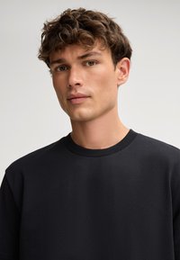 Zwarte crewneck-trui gemaakt van zachte stof. Heeft een eenvoudig ontwerp en een getextureerd oppervlak. Effent, zonder zichtbare logo's of patronen.