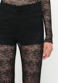 Black lace leggings with a floral pattern and a fitted waistband. The material is sheer, showing skin beneath the lace design.