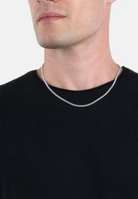 Silverfärgad kedjehalsband som bärs över en svart skjorta, med en slät, rund design och hopkopplade länkar med en polerad yta.