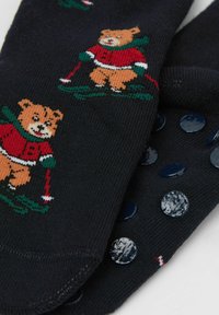 Calcetines de punto azul marino con un diseño de oso en rojo y verde. Puntos azules antideslizantes en la suela que mejoran el agarre.