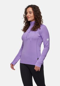 Leichtes lila Langarm-Sportoberteil mit einem halben Reißverschlusskragen, gerippter Textur und Logodetail am Ärmel. Kombiniert mit schwarzen Leggings.