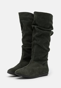 Bottes vertes en daim montant jusqu'au genou avec un design décontracté, bout pointu et semelle noire en caoutchouc basse, présentant une texture lisse et une coloration uniforme.