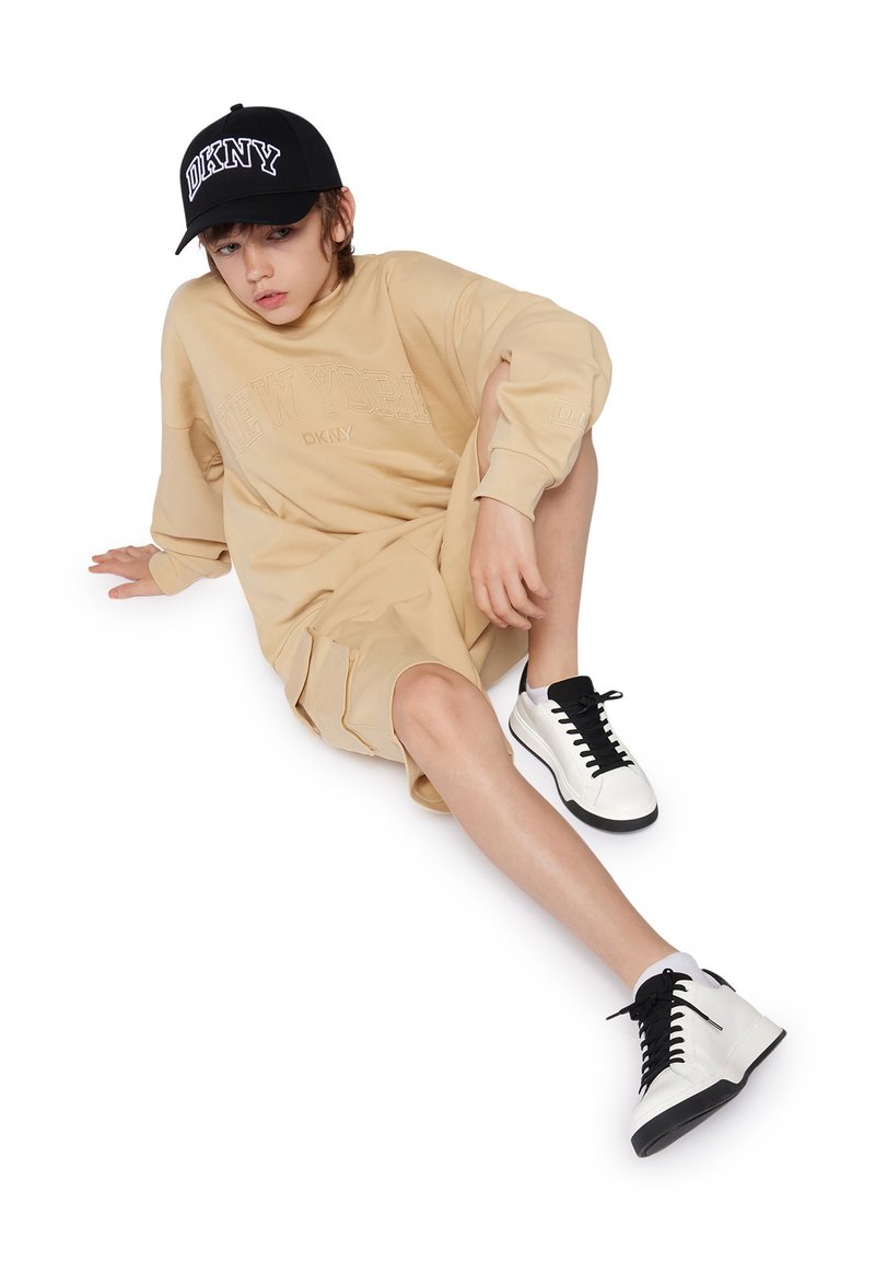 Vestido sudadera beige con estampado de "NEW YORK", combinado con gorra negra y zapatillas blancas con cordones negros y suela negra.