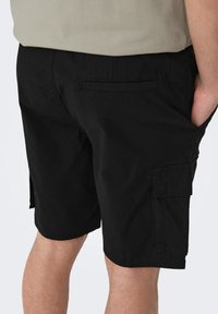 Pantaloni cargo neri realizzati in tessuto resistente, dotati di tasche laterali e orlo standard, con un design minimalista e senza motivi visibili.