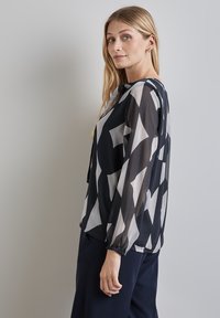 Schwarz-weiße gemusterte Bluse aus leichtem, durchsichtigem Material, mit langen Ärmeln und elastischen Bündchen sowie einem lockeren Schnitt.