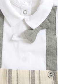 Chemise blanche en coton avec un nœud papillon gris et des bretelles rayées gris et beige. Comprend une fermeture pression et un détail de bouton.