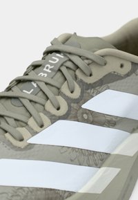 Green athletic shoe with gray floral pattern, white stripes, and textured upper. Features six lace holes and a padded collar.
