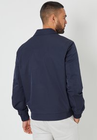 Marineblaue Jacke aus leichtem Stoff. Hat einen Kragen, elastische Bündchen und eine lockere Passform. Glatte Textur ohne sichtbare Muster.