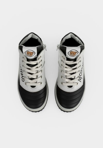 Paire de baskets montantes noires et blanches avec lacets, logo ours en peluche sur les languettes, et texte "Moschino" sur les côtés, vues de dessus.