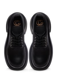 Black leather shoes featuring a rounded toe, thick sole, lace-up design with six eyelets, and embossed logo on the insole.