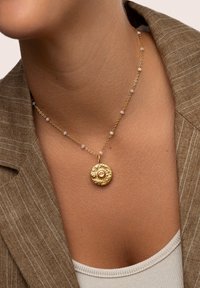 Goldene Anhänger-Halskette mit einem strukturierten runden Charm und Perlen, akzentuiert von kleinen hellrosa Perlen an einer zarten Kette.